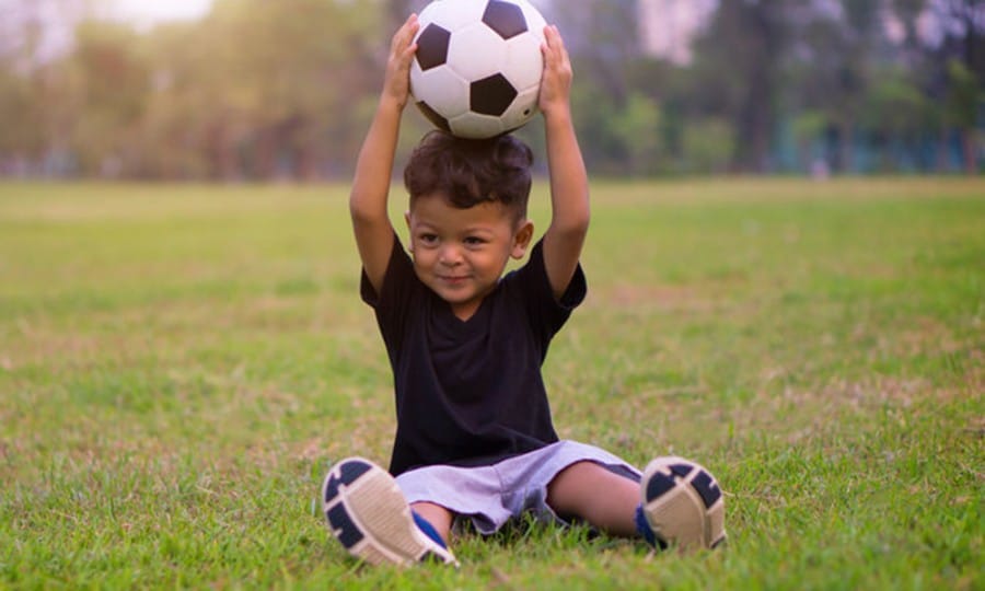 large motor activities using balls-young boy holding a soccer ball above his head in a park
