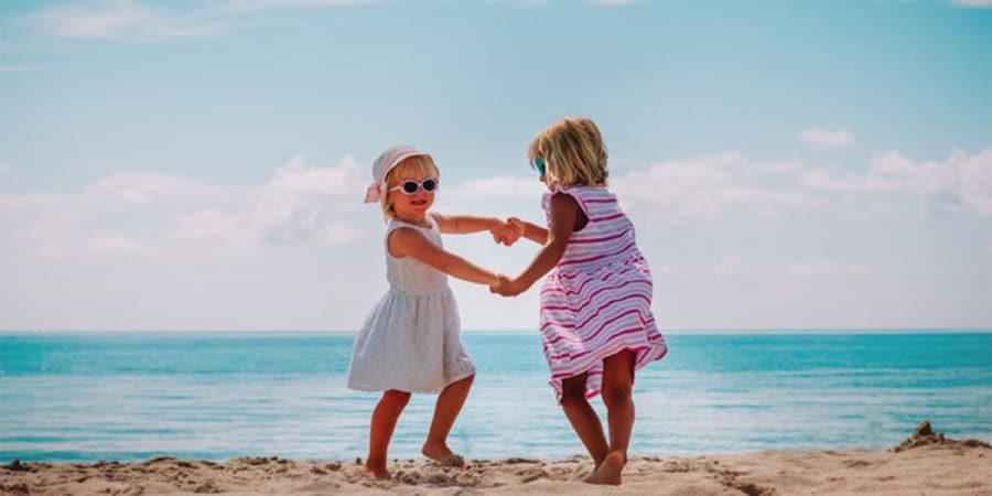 gross motor games-two young girls playing ring around the rosie on the beach
