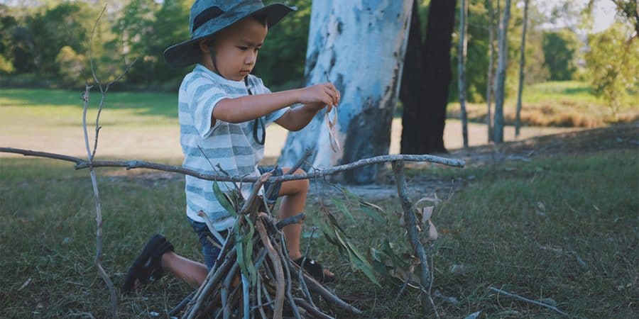 imaginative play- young boy playing outside creating a pretend campfire
