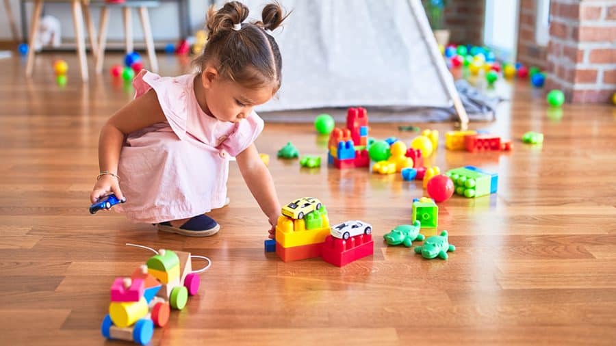blocks activities-young toddler girl playing with blocks, cars and other toys on the floor in a playroom