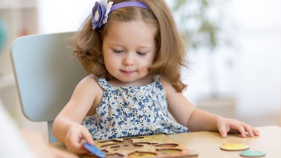 quiet activities for toddlers-toddler girl sitting in a chair at a table playing with a puzzle