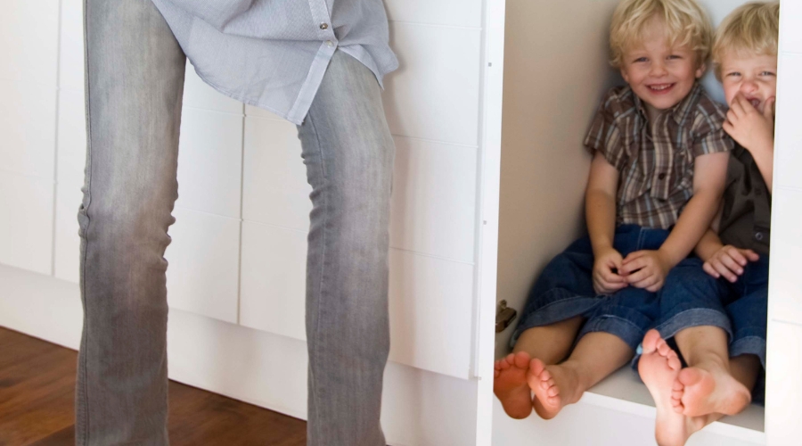 indoor activities for toddlers like hide and seek. two young boys are hiding from their mom in a closet. you can see the moms legs just right outside the door to the closet.