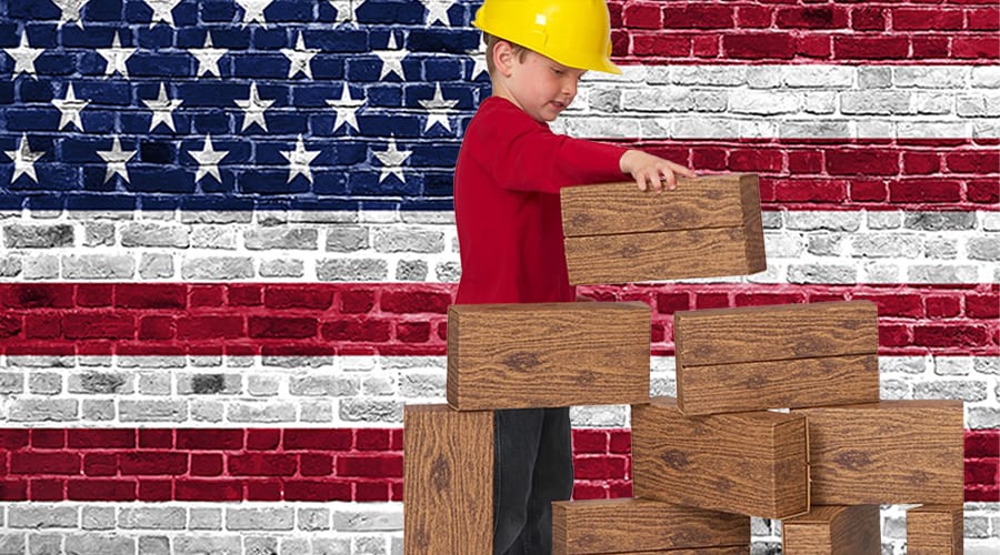 boy, wearing a hard hat, building with giant building blocks made in America, with a US flag background.